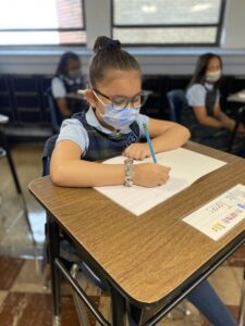 Girl holding pencil writes on paper